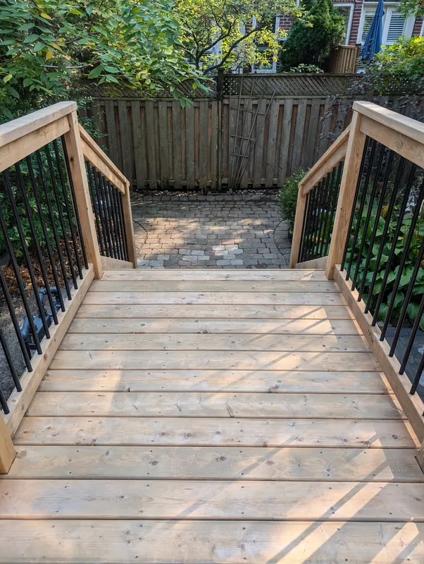 New deck stairs with black metal spindles leading to a stone patio